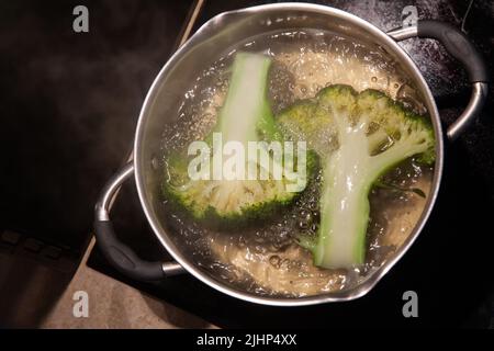 Längs geschnittene Brokkoli-Blütenstände werden in kochendem Wasser in einem Topf gekocht, Draufsicht aus der Nähe Stockfoto