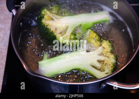 Die längs geschnittenen Brokkoli-Blütenstände werden in kochendem Wasser in einem Topf gekocht. Stockfoto