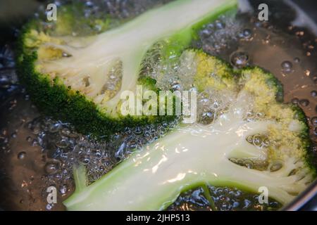 Brokkoli-Blütenstände, längs geschnitten, werden in kochendem Wasser in einem Topf gekocht, aus der Nähe Stockfoto