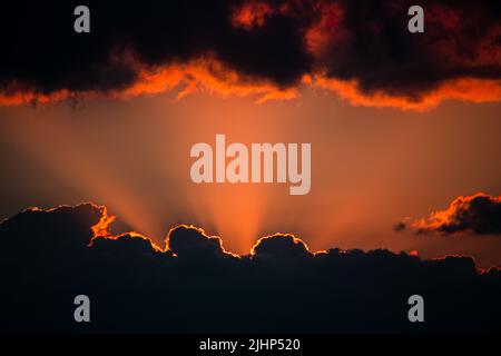 Sonnenuntergang. Von unten tauchen Lichtstrahlen aus den Wolken auf. Und Wolken hängen von oben. In der Mitte ist Platz für Text. Stockfoto