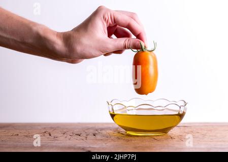 Olivenöl. Spanien Olivenöl in Glas transparente Schüssel mit Tomaten in der Hand. Nahaufnahme, isoliert auf weißem Hintergrund. Stockfoto