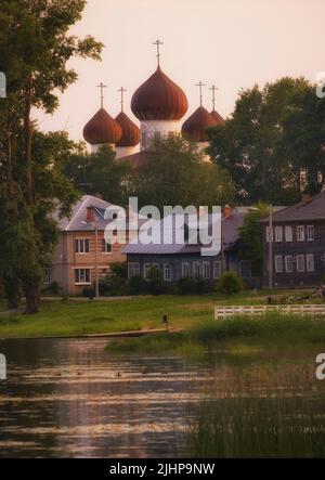 Niedliche Holzhäuser vor dem Hintergrund einer Kirche in der Nähe des Flusses Onega in der antiken Stadt Kargopol Stockfoto