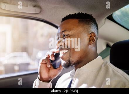 Schwarzer Geschäftsmann, der alleine in einem Taxi unterwegs ist, während er morgens mit seinem drahtlosen Smartphone auf dem Weg zur Arbeit im telefonieren muss Stockfoto