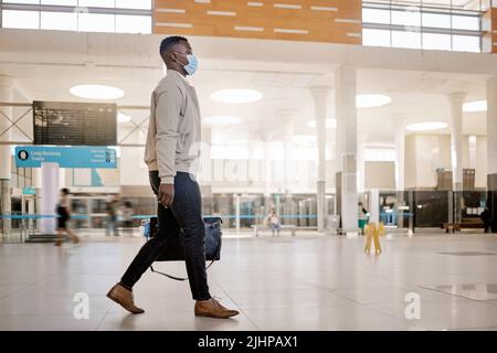 afroamerikanischer Geschäftsmann, der allein reist und in einem Bahnhof läuft, während er eine Maske zum Schutz vor Coronaviren trägt. Junger schwarzer Mann Stockfoto