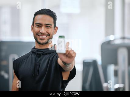 Porträt eines lächelnden Trainers allein in der Turnhalle, hält und zeigt eine Flasche Steroid-Pillen. Asiatischer Trainer mit hormonverstärkenden Medikamenten für das Training in Stockfoto