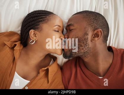 Nahaufnahme eines liebenden afroamerikanischen Paares, das sich von oben auf einem Bett küsst. Glücklicher junger Mann und Frau teilen romantische intime Stockfoto