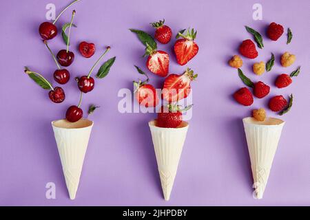 Spritzer Sommerbeeren aus Eiszapfen auf violettem Hintergrund. Sommer Essen flach lag. Stockfoto