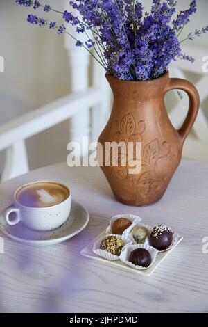 Sortierte vegane ohne Zuckertrüffel ohne Backen, Mehl und Milch. Tasse Cappuccino auf einem Holztisch im Café. Natürliche Süßigkeiten. Kaffeepause. Lavendel Stockfoto