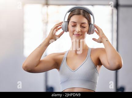 Eine aktive junge kaukasische Frau hört entspannende Musik mit Kopfhörern, während sie eine Pause vom Training im Fitnessstudio nimmt. Weibliche Sportlerin bleibt Stockfoto