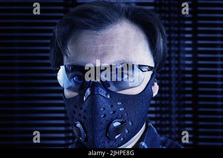 Ein Mann mittleren Alters mit Sonnenbrille und einer Atemmaske auf einem futuristischen Metallhintergrund. Futuristisches Porträt im industriell-technogenen Stil Stockfoto