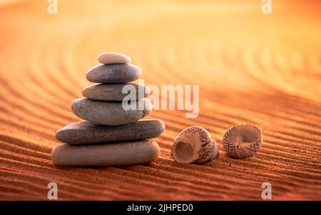 Stapel von sechs Zen-Steinen in einer entspannten Sonnenuntergangs-Strandumgebung, die Ruhe und Harmonie beschwört. Stockfoto