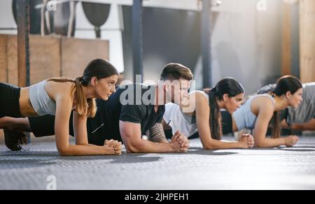 Verschiedene Gruppen von fit Menschen tun Bodyweight Plank halten Übungen zusammen in einem Fitnessstudio. Fokussierte Athleten trainieren, um Muskeln aufzubauen, den Oberkörper zu verbessern Stockfoto