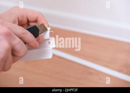 Ein Mann schneidet die Fußleisten auf eine geeignete Größe für die Installation in einem Raum. Renovierung des Hauses. Stockfoto