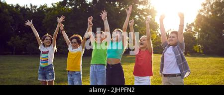 Fröhliche Kinder rufen bei der Unterhaltung im Sommerpark emotional und aufgeregt die Hände auf Stockfoto