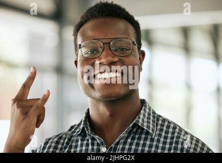 Junger afroamerikanischer Geschäftsmann mit einer Brille, die in einem Büro Horn oder Felsschild zeigt. Fröhlicher männlicher Unternehmer am Arbeitsplatz Stockfoto