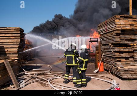 Hamburg, Deutschland. 20.. Juli 2022. Feuerwehrleute löschen ein brennendes Lagerhaus im Landkreis Altengamme. Die Halle, in der Landmaschinen und Holz gelagert wurden, war am Morgen in vollem Feuer. Quelle: Daniel Bockwoldt/dpa/Alamy Live News Stockfoto