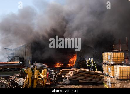 Hamburg, Deutschland. 20.. Juli 2022. Feuerwehrleute löschen ein brennendes Lagerhaus im Landkreis Altengamme. Die Halle, in der Landmaschinen und Holz gelagert wurden, war am Morgen in vollem Feuer. Quelle: Daniel Bockwoldt/dpa/Alamy Live News Stockfoto