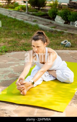 Junge Frau praktiziert Yoga im Garten. Yoga Pose Halb Gebunden Lotus Nach Vorne Sitzend Verlängerung. Ardha Padma Janushirshasana. Stockfoto