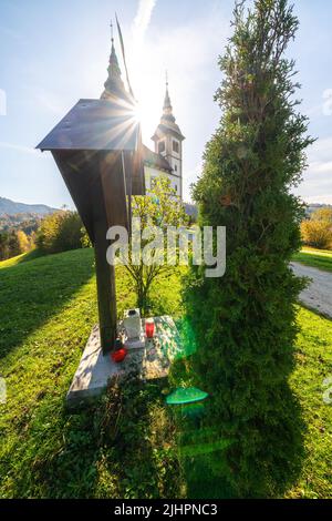 Blick auf das Kreuz vor der Kirche St. Volbenka in herbstlichen Farben vor blauem Himmel, Slowenien, Europa. Stockfoto