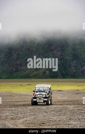 Japanischer klassischer Jeep FJ40 für den Transport von Touristen Parken allein am Mount Bromo im Tengger Semeru Nationalpark. Keine Personen. Nebel über dem Jeep. Stockfoto