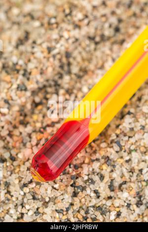 Glasthermometer mit roter Tinte auf grobem Sandhintergrund. Für die Sommerhitzewelle 2023 in Großbritannien, heißes Wetter, hohe Temperaturen, quecksilbersteigende Metapher. Stockfoto