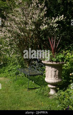 Gartenbank aus Metall und Urne im englischen Sommergarten Stockfoto