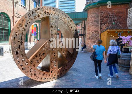Zwei Frauen gehen an einer Peace-Sign-Metallskulptur im Distillery District, Toronto, Ontario, Kanada, vorbei. Stockfoto