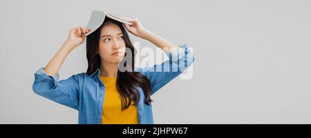 Schöne asiatische Frau langweilig und halten Buch auf dem Kopf, müde und gelangweilt junge Studentin Stockfoto