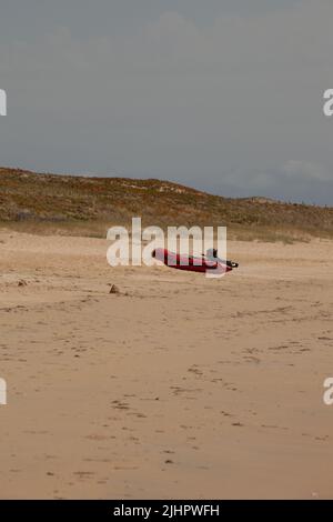 Ein rotes Schlauchboot ist am Strand, vor der Düne. Stockfoto