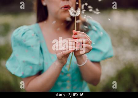 Glückliche Frau schön weht auf Dandelion im Park. Mädchen in vintage blauen Kleid. Wishing, Joy Konzept. Frühling, ästhetisches Porträt Stockfoto