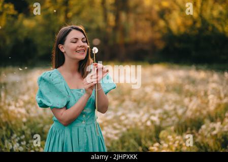 Glückliche Frau schön weht auf Dandelion im Park. Mädchen in vintage blauen Kleid. Wishing, Joy Konzept. Frühling, ästhetisches Porträt Stockfoto