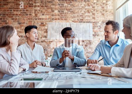 Eine Gruppe verschiedener Architekten diskutiert während eines Meetings in ihrem Sitzungssaal Pläne, Pläne und Schaltpläne. Geschäftsleute Brainstorming und Stockfoto