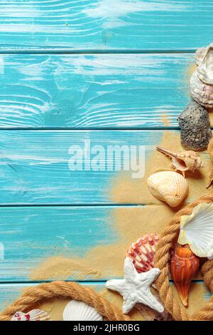 Meer Seil mit vielen verschiedenen Muscheln auf dem Meer Sand auf einem blauen Hintergrund aus Holz. Ansicht von oben Stockfoto