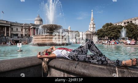 Während der Hitzewelle in London sonnen sich Touristen am Trafalgar Square-Brunnen. Stockfoto