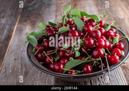 Schüssel mit frisch gepflückten Sauerkirschen. Serviert in einer braunen Emaille-Schüssel isoliert auf einem Holztisch mit Kopierbereich Stockfoto