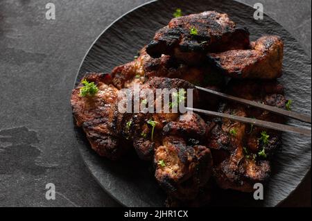 Grillen Sie Schweinesteaks auf einem Teller, der auf dunklem Tischhintergrund isoliert ist Stockfoto