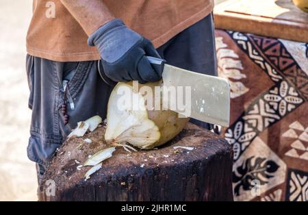 Ein Mann, der eine Kokosnuss schneidet, um frische Kokosmilch in Hawaii zu bekommen, während er im Urlaub ist Stockfoto