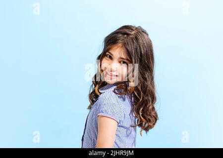 Portrait von Winsome kleines Mädchen, Schulalter Kind im Sommerkleid isoliert auf blauem Hintergrund. Konzept der Kinder Emotionen, Mode, Schönheit, Schule Stockfoto