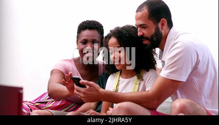 Multiethnische Familie mit Mobiltelefon. Interrassische Eltern und Kinder mit gemischter Rasse, die gemeinsam auf den Smartphone-Bildschirm schauen Stockfoto