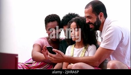 Multiethnische Familie mit Mobiltelefon. Interrassische Eltern und Kinder mit gemischter Rasse, die gemeinsam auf den Smartphone-Bildschirm schauen Stockfoto