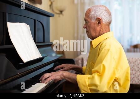 Mann, der im Wohnzimmer seines Heims Klavier spielt, nachdem er sich von der Arbeit verabschiedet hat Stockfoto