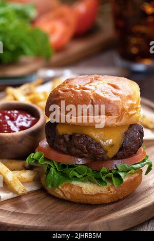 Cheeseburger mit Salat und Tomaten auf geröstetem Brötchen mit pommes Frites und Ketchup auf Holzplatte Stockfoto