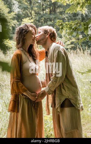 Seitenansicht des Mannes, der lächelnde, Schwangere im Wald küsst Stockfoto