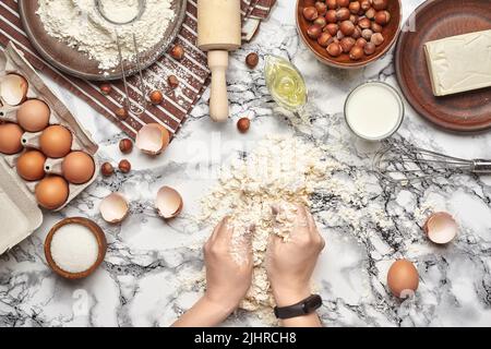 Nahaufnahme. Draufsicht auf einen Bäckerkochplatz, Hände arbeiten mit einem rohen Teig auf dem Marmortisch Hintergrund. Stockfoto