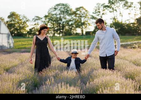 Fröhliche Familie, die mit den Händen ihres Sohnes durch das Lavendelfeld läuft Stockfoto