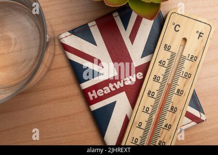 UK Heatwave Concept: Leder-Geldbörse mit Union Jack Flagge und einem Thermometer auf einem Holztisch Stockfoto