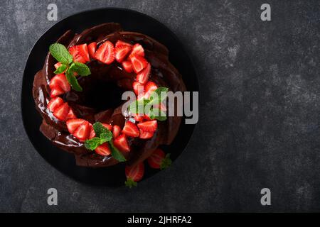 Dunkler Schokoladenkuchen mit Ganache-Vereisung und Erdbeere auf dunklem Stein- oder Betontischhintergrund. Festlicher Kuchen. Selektiver Fokus Stockfoto