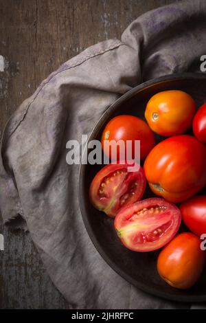 Haufen Tomaten auf einem Teller, frisch geerntete rote Beeren auf einer Holzoberfläche, von oben genommen Stockfoto