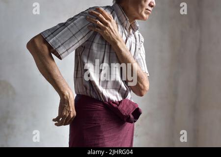 Steifheit im Schultergelenk des südostasiatischen älteren Mannes. Konzept der gefrorenen Schulter- oder Armmuskelkraftprobleme. Stockfoto