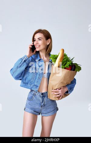 Frau mit Papiertüte mit Gemüse und Smartphone Stockfoto
